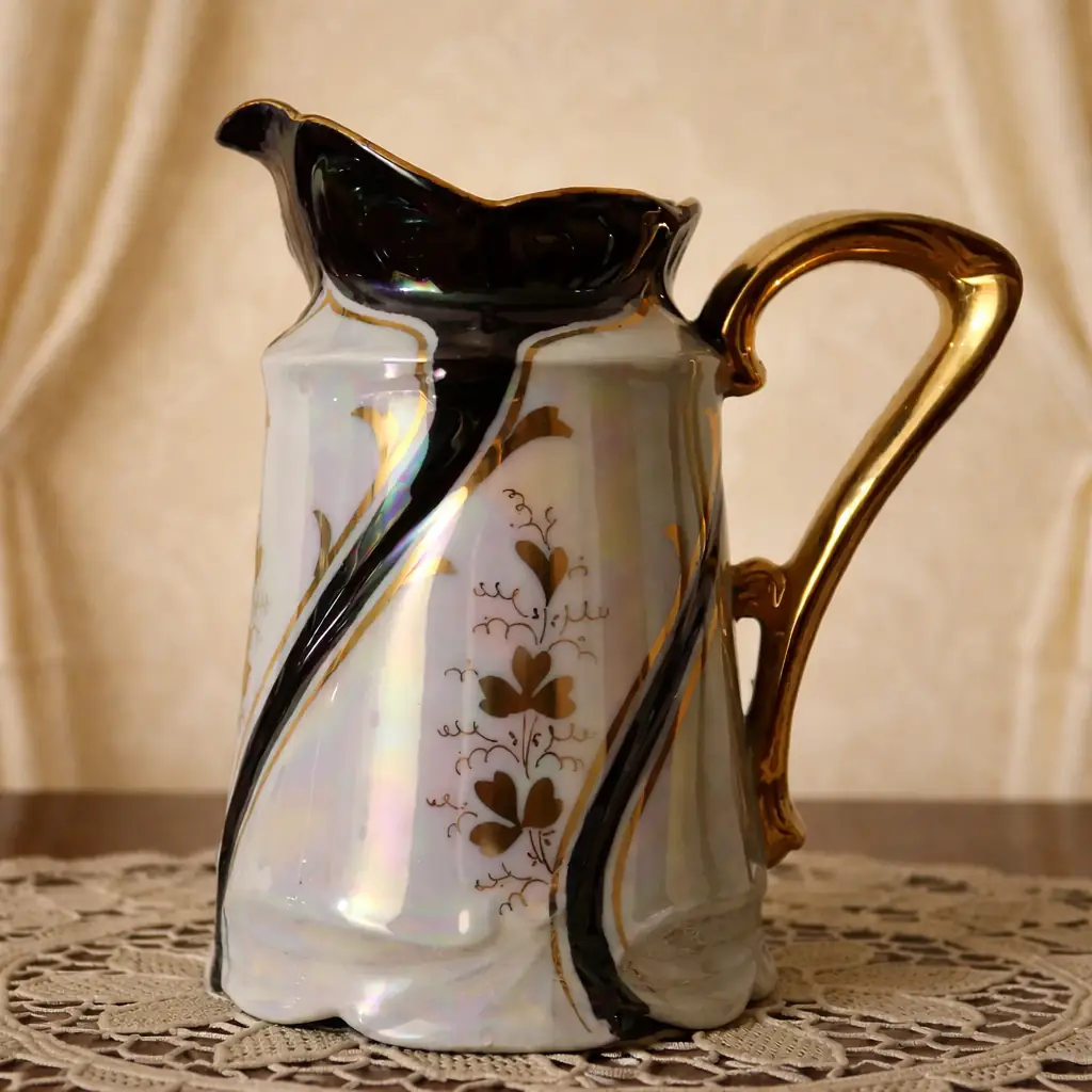 Servizio da caffè in porcellana iridescente con finiture in oro – 15 pezzi Raffinato servizio da caffè in porcellana europea della prima metà del Novecento, caratterizzato da una luminosa finitura madreperlata con eleganti riflessi cangianti nei toni del viola e del verde. Il decoro floreale stilizzato, eseguito in oro, si integra armoniosamente alle linee mosse e slanciate delle forme, di gusto Liberty. Il servizio è composto da 12 tazzine con relativi piattini, caffettiera con coperchio, lattiera e zuccheriera con coperchio. I manici dorati e i dettagli finemente modellati conferiscono all’insieme grande eleganza e ricercatezza. Marchio al verso con corona. Ottimo stato di conservazione, con lievi segni del tempo coerenti con l’epoca. Ideale per collezione o per impreziosire una tavola d’atmosfera.