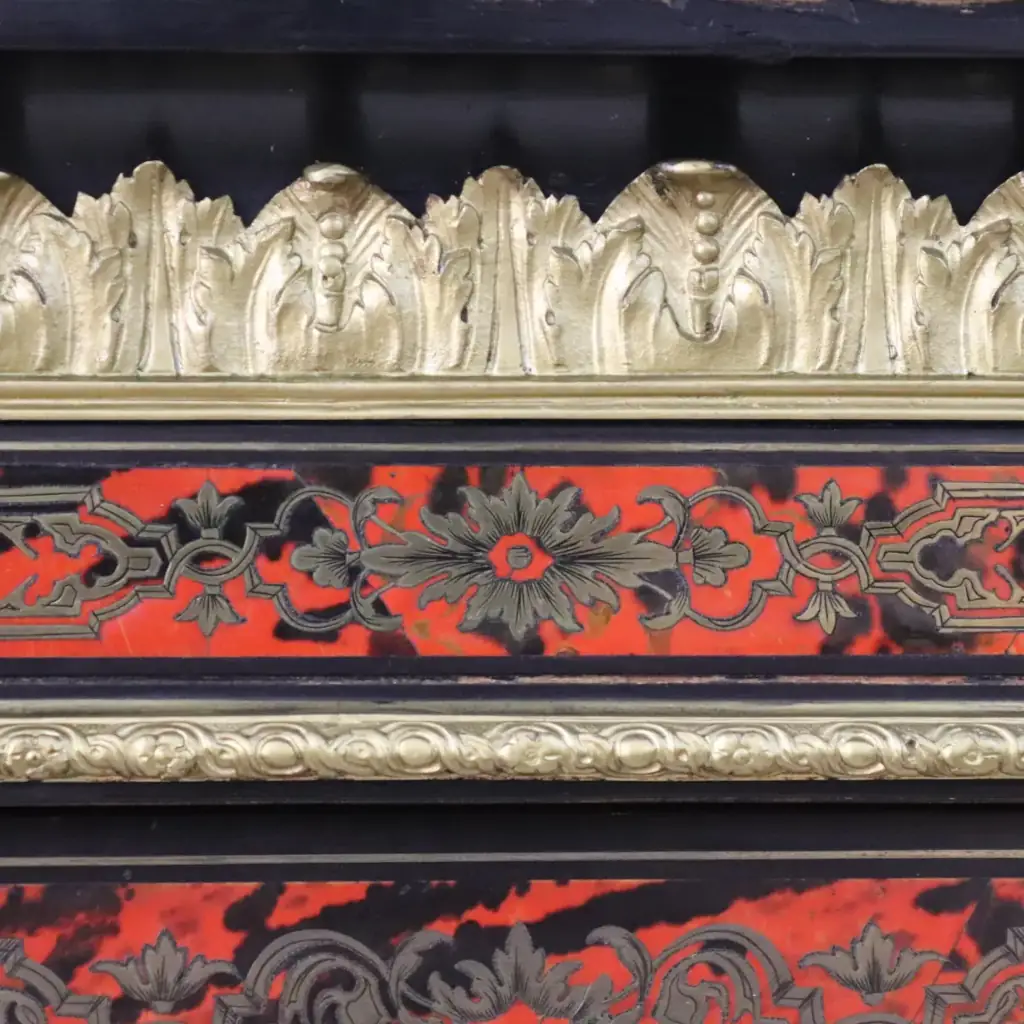 Vetrina alla Boulle in ebano, tartaruga e bronzi dorati Francia, seconda metà del XIX secolo – Stile Napoleone III Raffinata vetrina a un’anta realizzata secondo la celebre tecnica “alla Boulle”, con impiallacciatura in ebano e ricchi intarsi in ottone su fondo in tartaruga rossa naturale, disposti in eleganti motivi a racemi e volute di gusto Luigi XIV. Il prospetto è impreziosito da importanti applicazioni in bronzo dorato finemente cesellato, raffiguranti figure allegoriche laterali, fregi a foglie d’acanto e mascherone centrale nella parte inferiore. L’anta vetrata, incorniciata da profili dorati, apre su ripiani interni destinati all’esposizione di porcellane e oggetti d’arte. Esempio di alta ebanisteria francese del periodo Napoleone III, il mobile coniuga ricchezza ornamentale, equilibrio architettonico e forte impatto scenografico, risultando ideale per ambienti di rappresentanza o collezioni antiquarie di pregio.