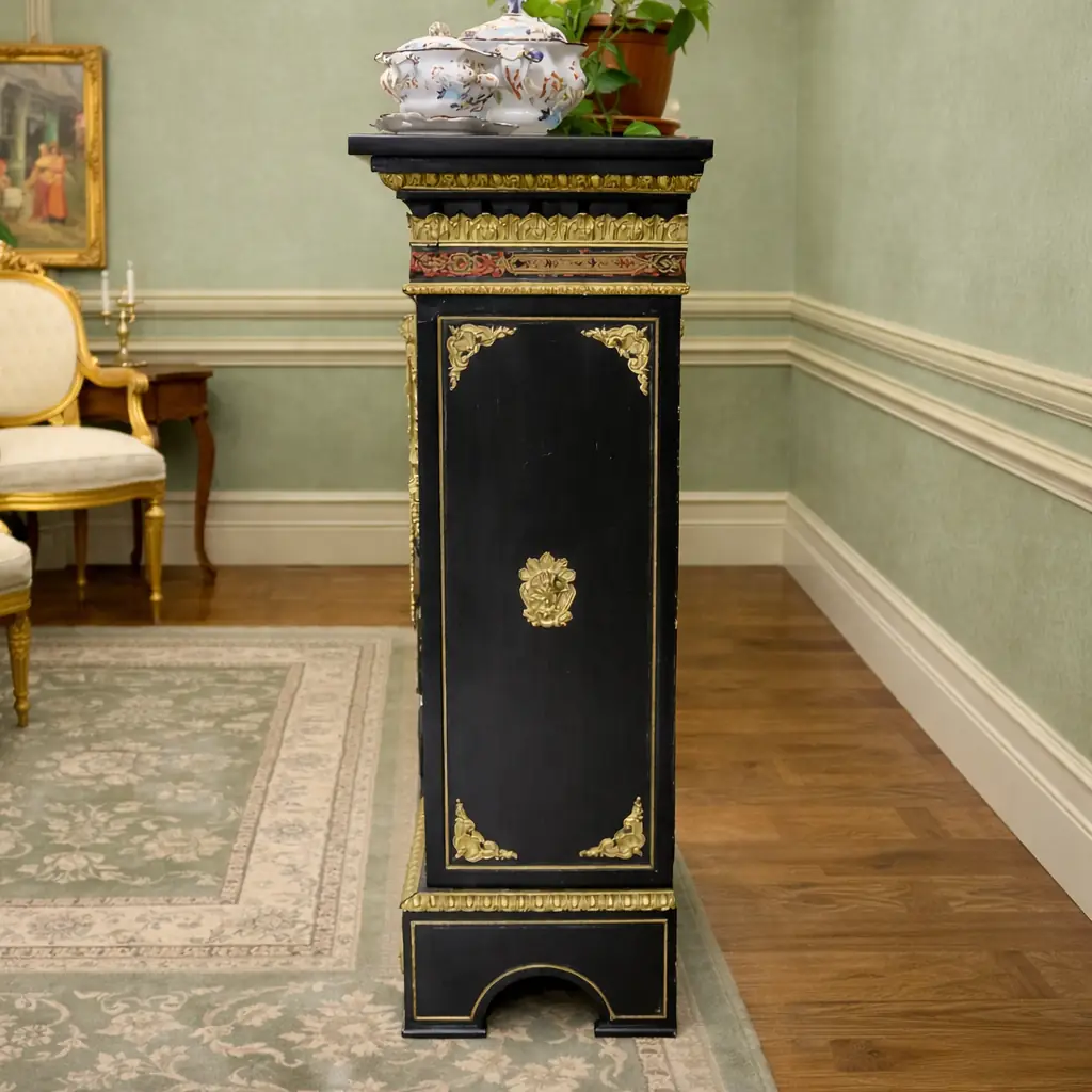 Vetrina alla Boulle in ebano, tartaruga e bronzi dorati Francia, seconda metà del XIX secolo – Stile Napoleone III Raffinata vetrina a un’anta realizzata secondo la celebre tecnica “alla Boulle”, con impiallacciatura in ebano e ricchi intarsi in ottone su fondo in tartaruga rossa naturale, disposti in eleganti motivi a racemi e volute di gusto Luigi XIV. Il prospetto è impreziosito da importanti applicazioni in bronzo dorato finemente cesellato, raffiguranti figure allegoriche laterali, fregi a foglie d’acanto e mascherone centrale nella parte inferiore. L’anta vetrata, incorniciata da profili dorati, apre su ripiani interni destinati all’esposizione di porcellane e oggetti d’arte. Esempio di alta ebanisteria francese del periodo Napoleone III, il mobile coniuga ricchezza ornamentale, equilibrio architettonico e forte impatto scenografico, risultando ideale per ambienti di rappresentanza o collezioni antiquarie di pregio.