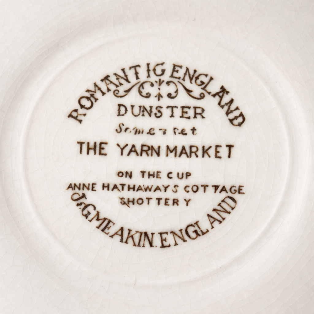 Tazza con piattino in ceramica – “Romantic England”, Staffordshire Tazza con piattino in ceramica inglese decorata con vedute paesaggistiche tratte dalla serie “Romantic England”, come da marchio al verso. I soggetti raffigurano scorci tradizionali britannici, tra cui Dunster (The Yarn Market) e Anne Hathaway’s Cottage a Shottery, resi in tonalità seppia con delicati accenti policromi. La forma è semplice ed elegante, con tazza leggermente svasata e ansa lineare; il bordo di entrambi i pezzi è impreziosito da una sottile filettatura rosso mattone che incornicia le scene. Esempio rappresentativo della produzione ceramica inglese del XX secolo, in buone/ottime condizioni di conservazione, ideale per collezionisti di oggetti a tema britannico o per arricchire una tavola con un tocco di fascino tradizionale.
