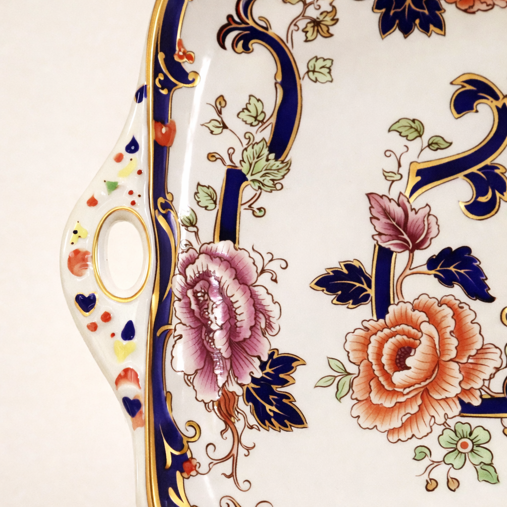 Vassoio con manici – Mason’s “Mandalay” Inghilterra, prima metà del XIX secolo Elegante vassoio da portata in porcellana inglese con manici laterali sagomati, produzione Mason’s Patent Ironstone, decoro “Mandalay”. La forma quadrangolare con angoli arrotondati è impreziosita da una ricca bordura blu cobalto profilata in oro, che incornicia un raffinato motivo floreale policromo di gusto orientale, con peonie e tralci stilizzati. Decorazione stampata e rifinita a mano; marchio al verso “Mason’s – Patent Ironstone – Mandalay – Made in England”, riferibile alla produzione della seconda metà del Novecento. In eccellente stato di conservazione, senza difetti evidenti. Oggetto di grande eleganza, ideale per una tavola importante o per arricchire una collezione di porcellane inglesi.