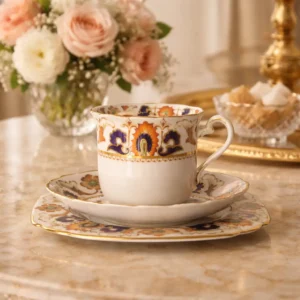TUSCAN CHINA – Longton, Staffordshire Trio da tè in porcellana fine, ca. 1930–1950 Raffinato trio da tè composto da tazza, piattino e piatto dessert coordinato, in porcellana inglese di produzione Tuscan China, con marchio al verso in verde “Tuscan China – Made in England”. La decorazione, di gusto Imari reinterpretato, presenta motivi floreali e volute stilizzate in rosso ferro e blu cobalto, impreziosite da tocchi in verde e ricche profilature in oro zecchino. Il piatto è elegantemente sagomato con angoli arrotondati e bordo dorato; la tazza, leggermente svasata, è dotata di ansa sagomata con filettatura in oro. Esemplare di grande impatto cromatico e qualità esecutiva, in ottimo stato di conservazione con minimi e fisiologici segni del tempo. Ideale per collezionisti di porcellane inglesi del Novecento o per una mise en place di gusto classico ed elegante.
