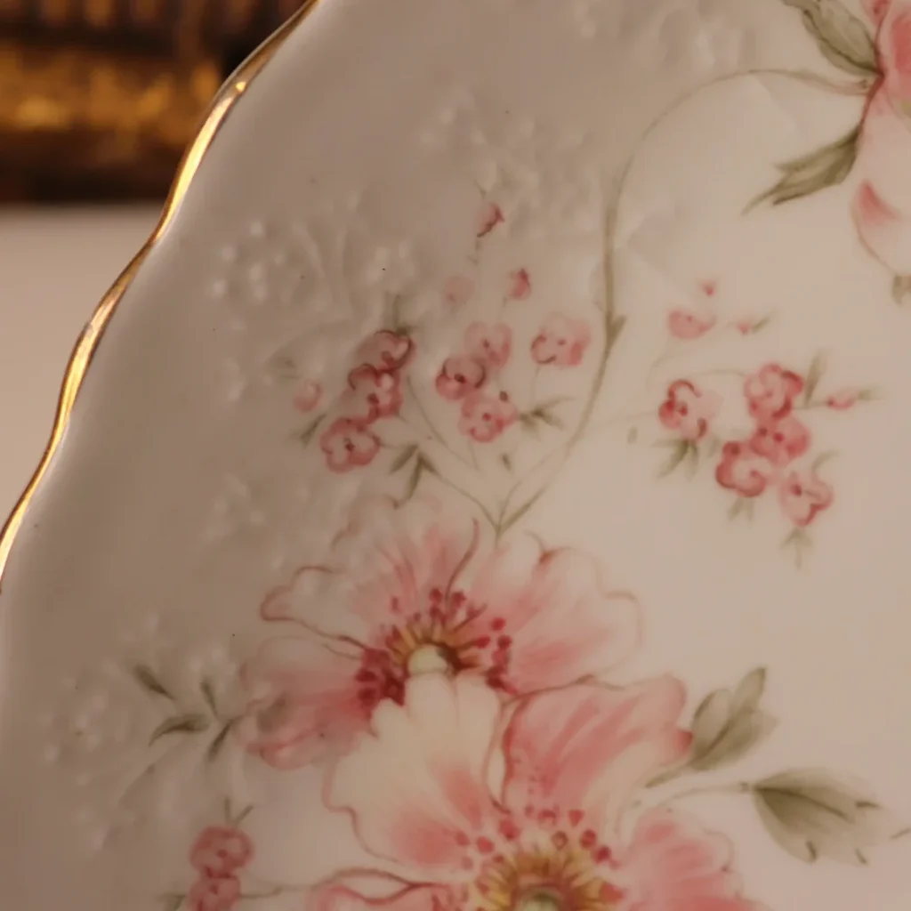 Royal Albert “Breath of Spring” – Piatto da dolce a trifoglio Delizioso piatto da dolce a forma di trifoglio della celebre collezione Breath of Spring di Royal Albert, realizzato in pregiata Bone China inglese. La particolare forma trilobata, con tre scomparti e raffinato manico centrale, lo rende un oggetto originale e ricercato, perfetto per presentare con eleganza pasticcini, biscotti, confetti e piccole prelibatezze. La delicata decorazione floreale nei toni del rosa, impreziosita da profilature dorate e raffinati rilievi ornamentali, dona alla porcellana un fascino romantico e tipicamente inglese. Un piccolo gioiello della tavola, capace di trasformare anche un semplice tè pomeridiano in un momento speciale. Perfetto da utilizzare, esporre o aggiungere a una collezione di porcellane Royal Albert. Royal Albert Bone China – Made in England – “Breath of Spring”. Un pezzo originale e pieno di charme, ideale per chi ama la raffinata eleganza delle porcellane inglesi.