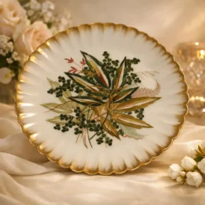 Elegante alzatina in porcellana di gusto tardo Ottocento / primi Novecento, caratterizzata da piatto sagomato con bordo ondulato e profilo dorato. La superficie è finemente decorata a motivo botanico centrale con foglie e bacche policrome, eseguite con pennellata delicata e naturalistica. Il fusto centrale poggia su una base sagomata, arricchita da elementi plastici e dorature a pennello, che conferiscono equilibrio e raffinatezza all’insieme. Oggetto da tavola o da centro, di pregiata manifattura europea, ideale come alzatina da esposizione o servizio dolci, in ottimo stato di conservazione.