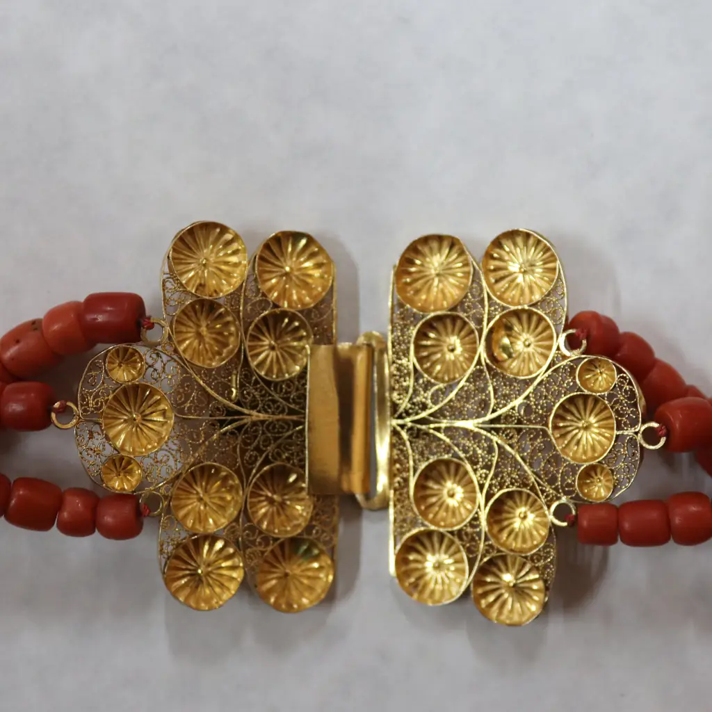 Raffinata collana a tre fili in corallo rosso mediterraneo naturale, composta da perle cilindriche accuratamente calibrate e caratterizzata da una splendida chiusura a cassetta in oro giallo, finemente lavorata a filigrana e impreziosita da un elegante motivo floreale inciso. Il caldo colore del corallo, unito alla preziosità della filigrana, crea un gioiello di grande presenza, luminosità e fascino mediterraneo, espressione della raffinata tradizione orafa italiana della seconda metà del XX secolo. In ottimo stato di conservazione, è un gioiello importante e ricercato, ideale per chi desidera indossare un pezzo dalla forte personalità o arricchire una collezione di gioielleria italiana. Peso complessivo: 116 g.